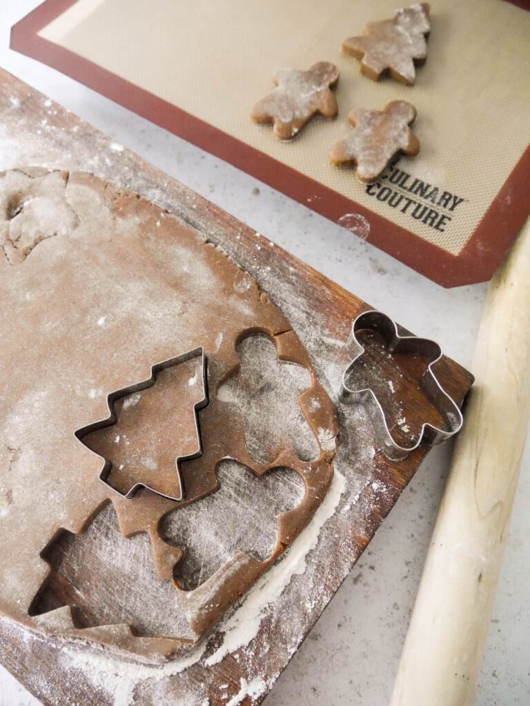 A sheet of rolled cookie dough set on a floured surface with cookie cutter with some cut cookies set on a baking sheet.