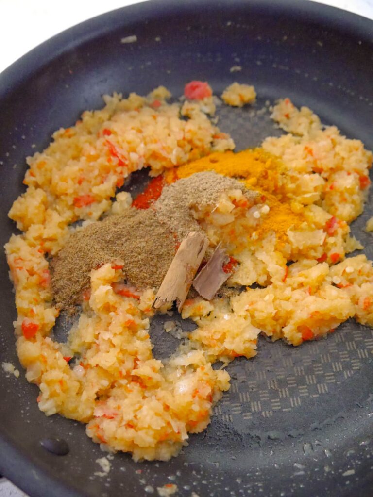 A frying pan filled with cooked onion and garlic with added dry spices.