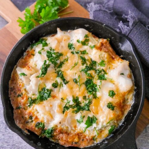 A cast iron skillet filled with omelette Arnold Bennett and topped with chopped parsley, set on a wooden board.