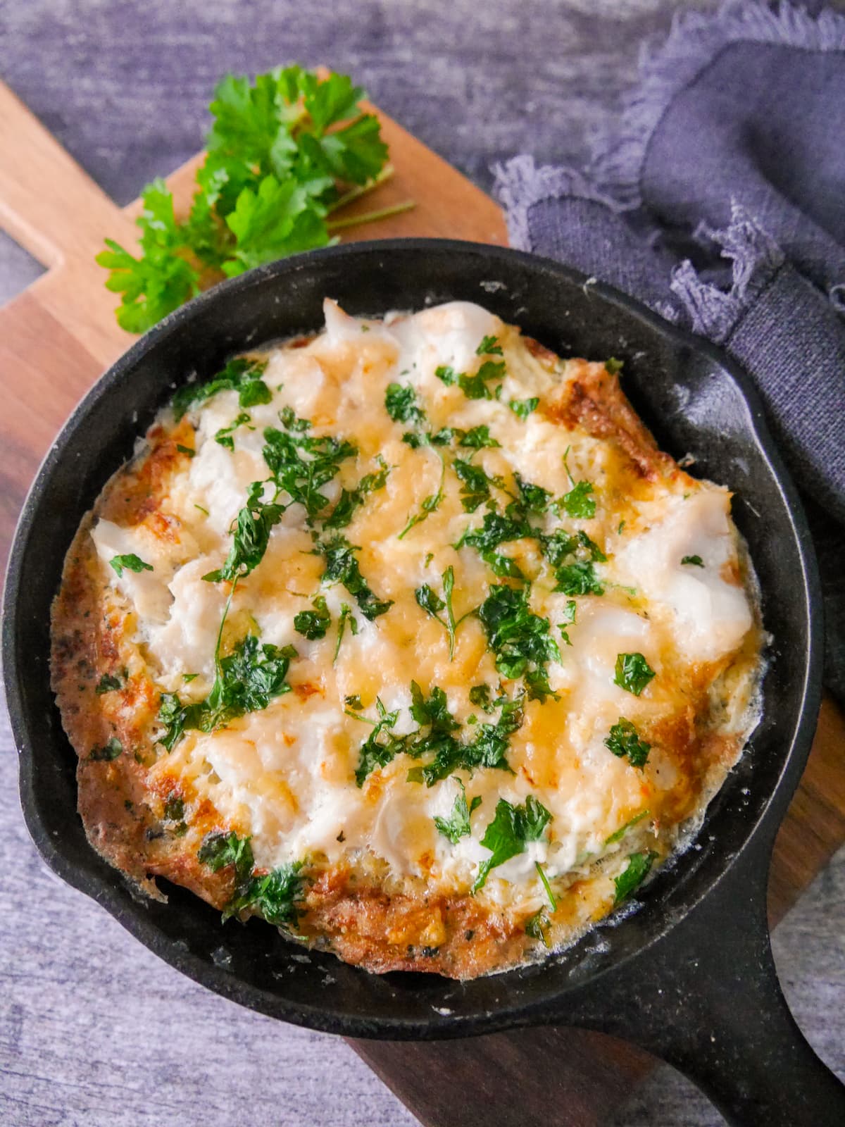 A cast iron skillet filled with omelette Arnold Bennett and topped with chopped parsley, set on a wooden board.