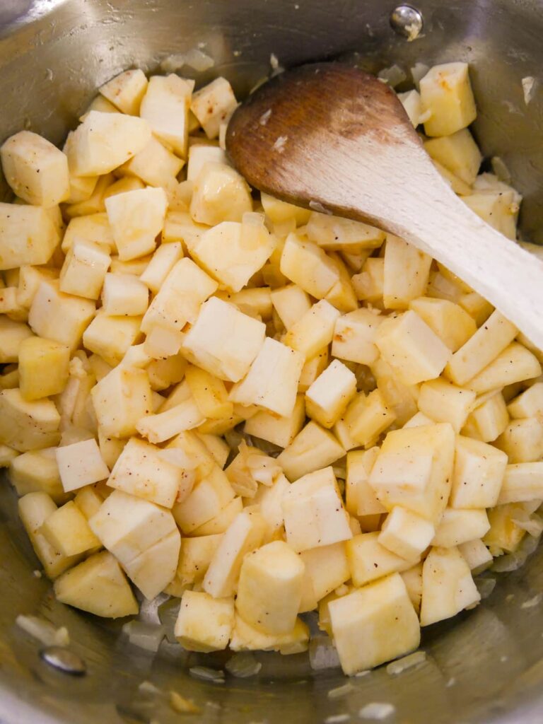 A saucepan of sauteed onion with added chunks of parsnip.