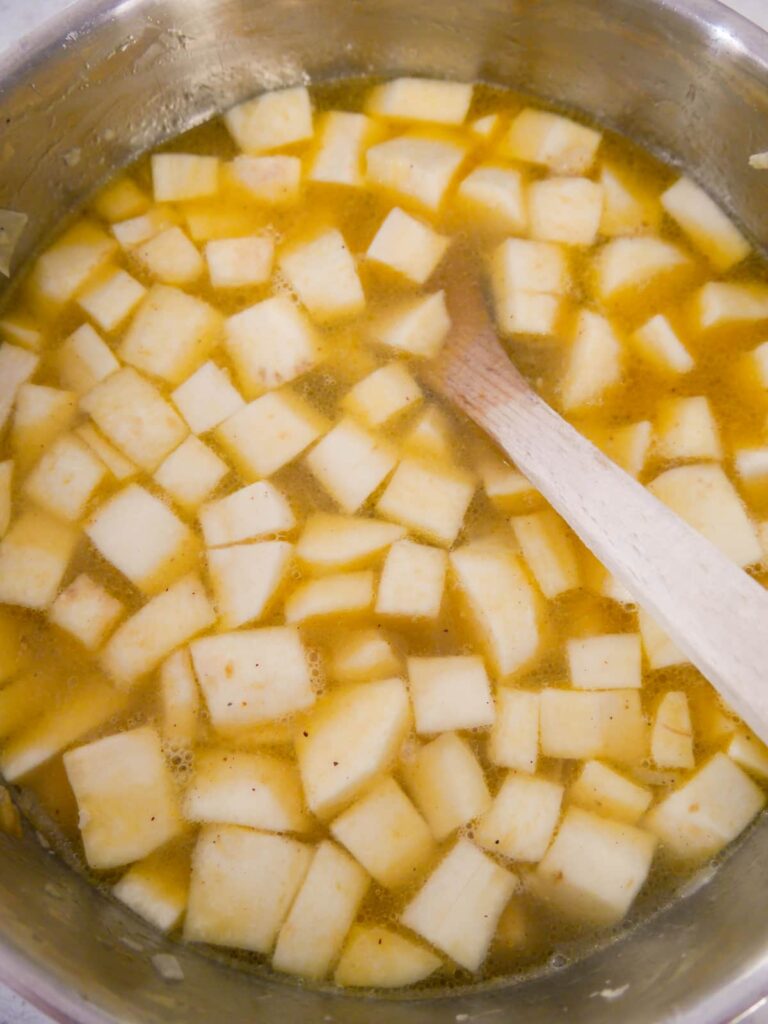 A saucepan of sauteed onion, garlic and parsnip with added vegetable stock.