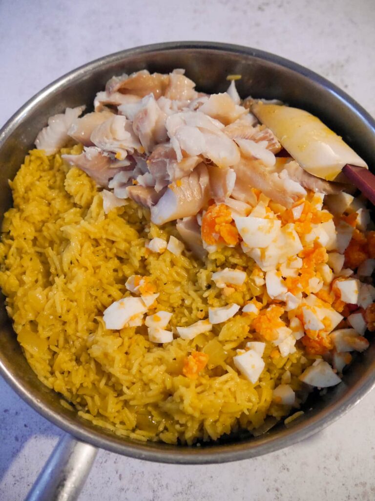 Smoked haddock pieces and chopped egg being added to a frying pan of seasoned rice.