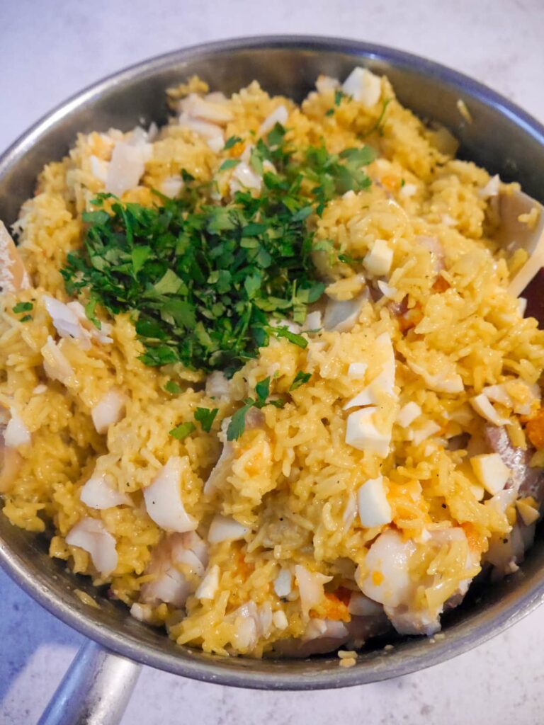 A frying pan filled with lighting spiced rice, chopped egg and smoked haddock pieces with added chopped parsley.