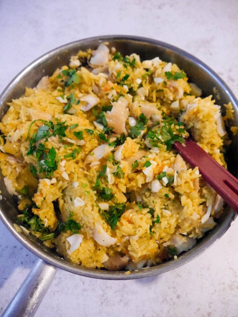 A frying pan filled with lighting spiced rice with added chopped egg, smoked haddock pieces and fresh parsley stirred through.