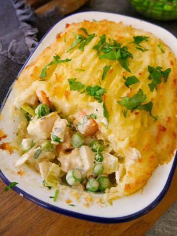 A portion of creamy fish pie with vegetables and a mashed potato topping, garnished with fresh parsley.