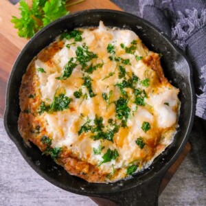 A cast iron skillet filled with omelette Arnold Bennett and topped with chopped parsley, set on a wooden board.