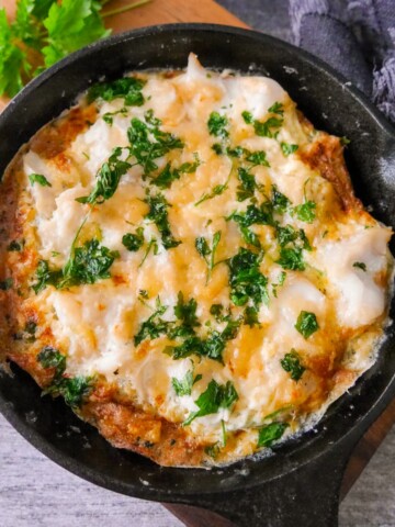 A cast iron skillet filled with omelette Arnold Bennett and topped with chopped parsley, set on a wooden board.