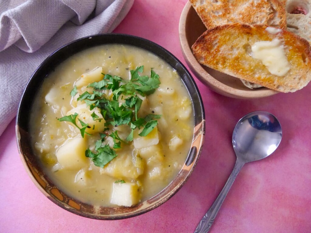 A bowl of rustic leek and potato soup topped with a garnish of chopped parsley, with a side of buttered toast.