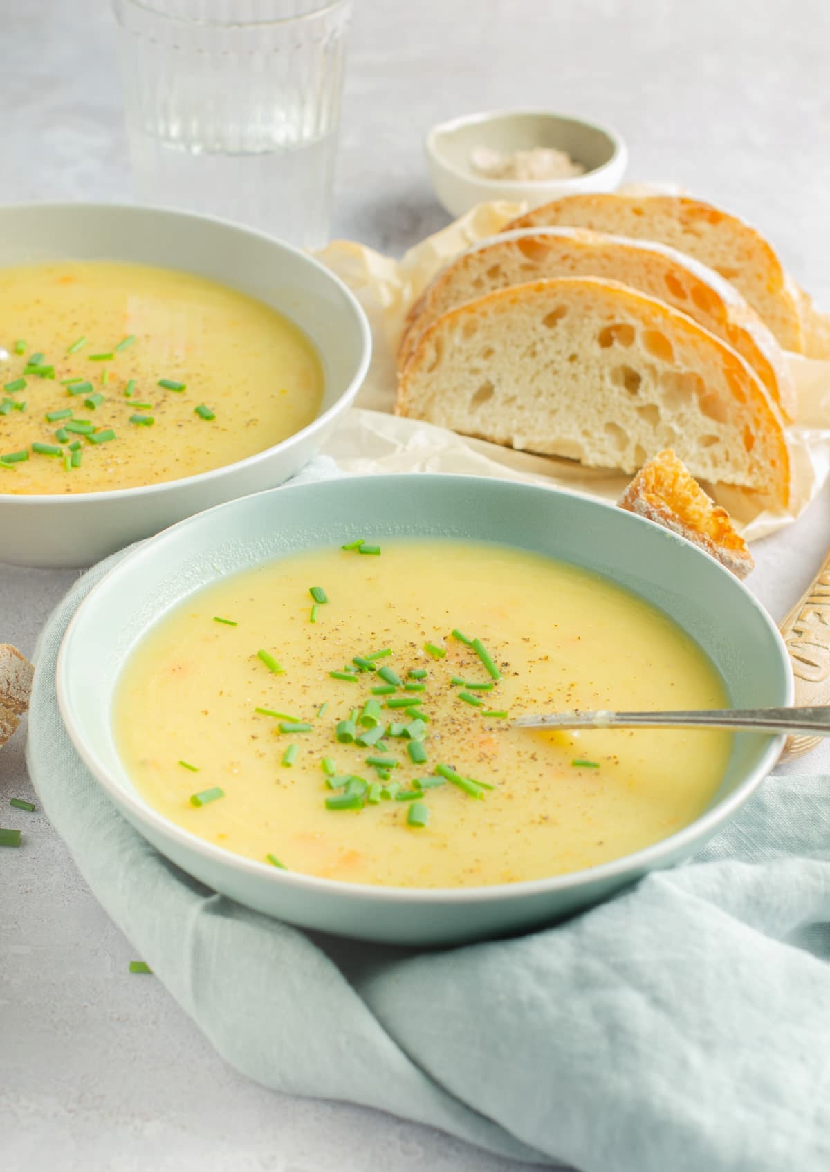 Two bowls of smooth/pureed leek and potato soup with a side of sliced crusty bread.