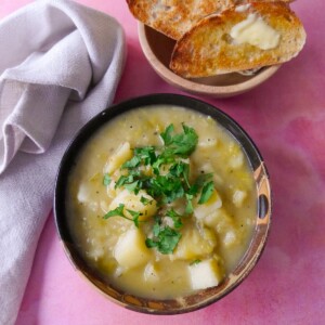 A bowl of rustic leek and potato soup topped with a garnish of chopped parsley, with a side of buttered toast.