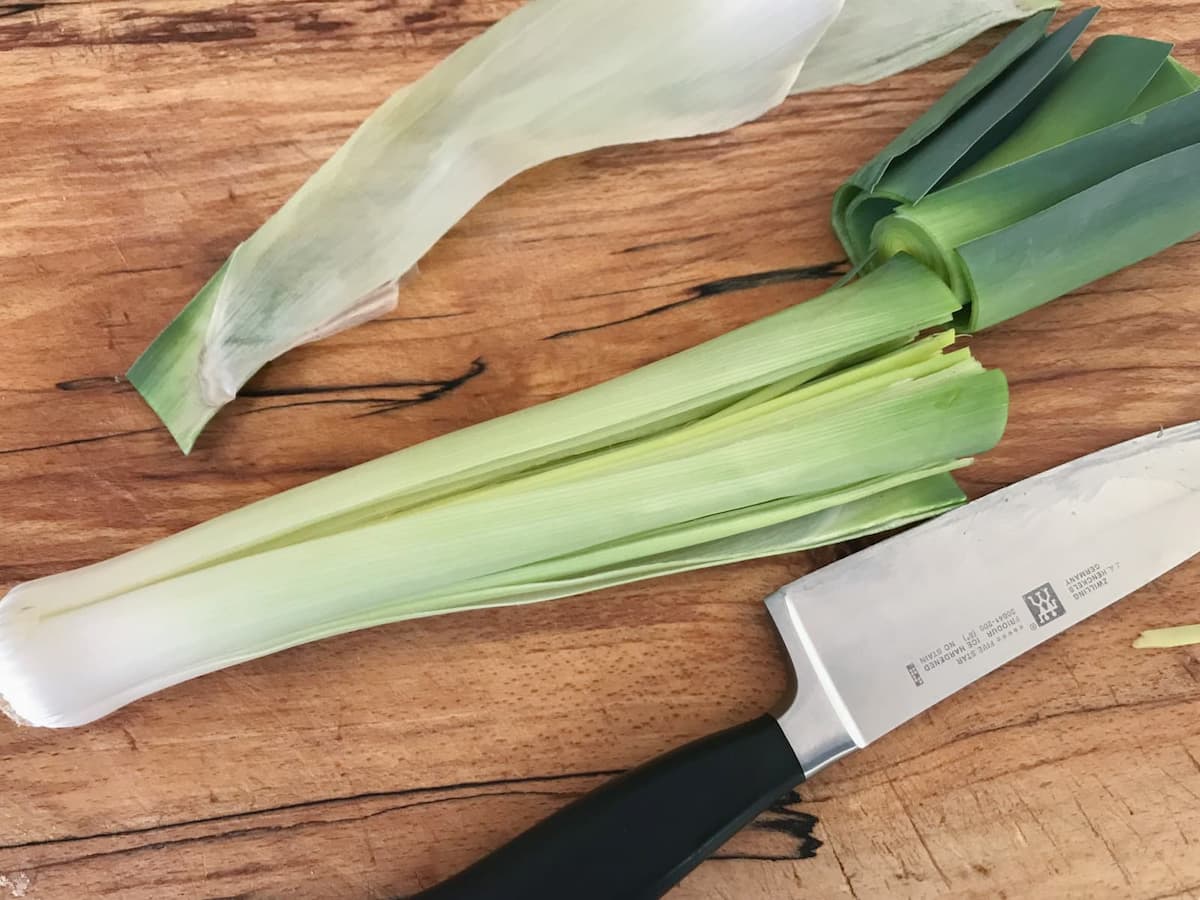 A chopping board with a quartered leek, with the green part and outer leaves removed.