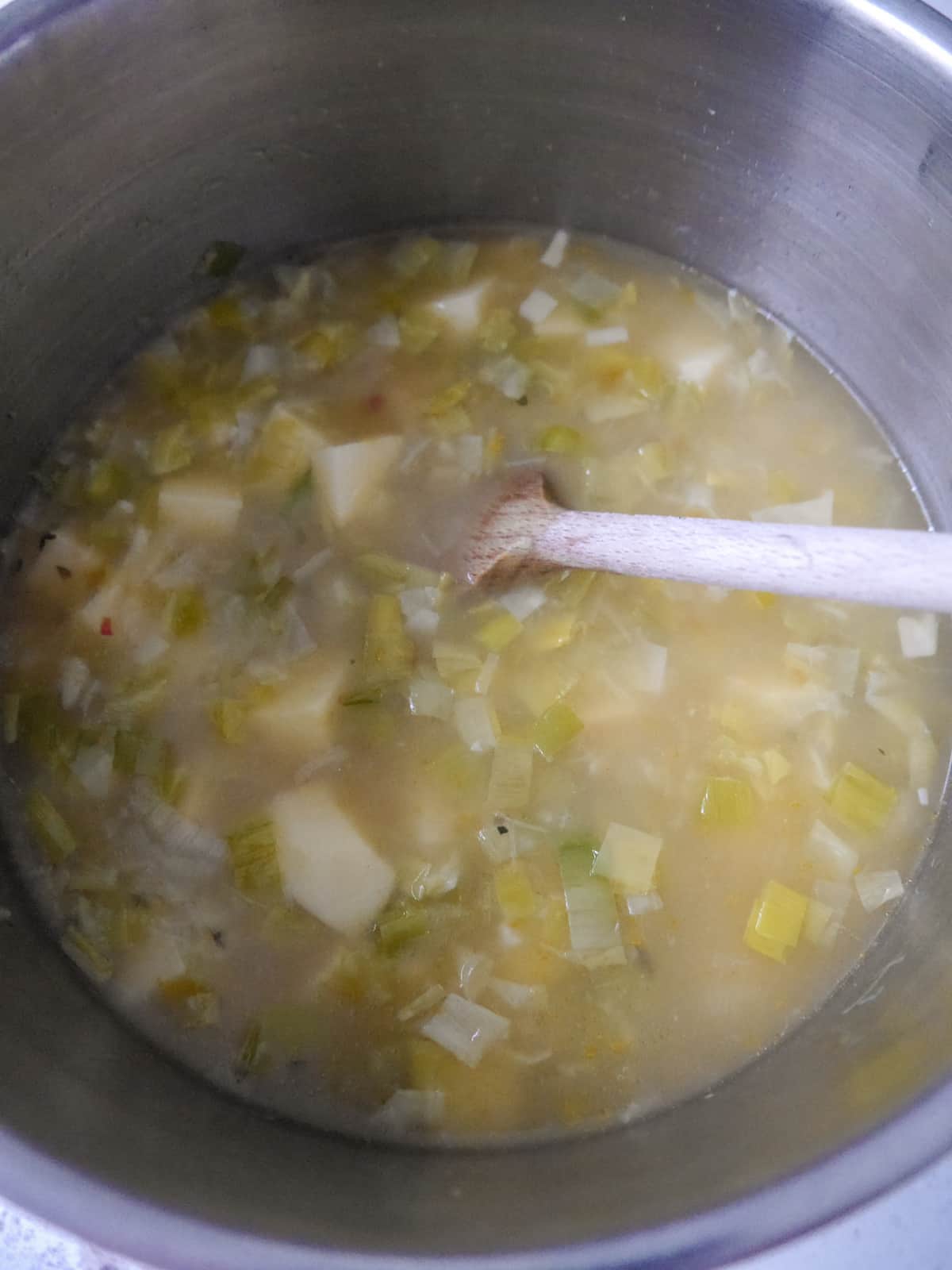 A saucepan filled with sauteed leeks and garlic with added chopped potato and vegetable stock.