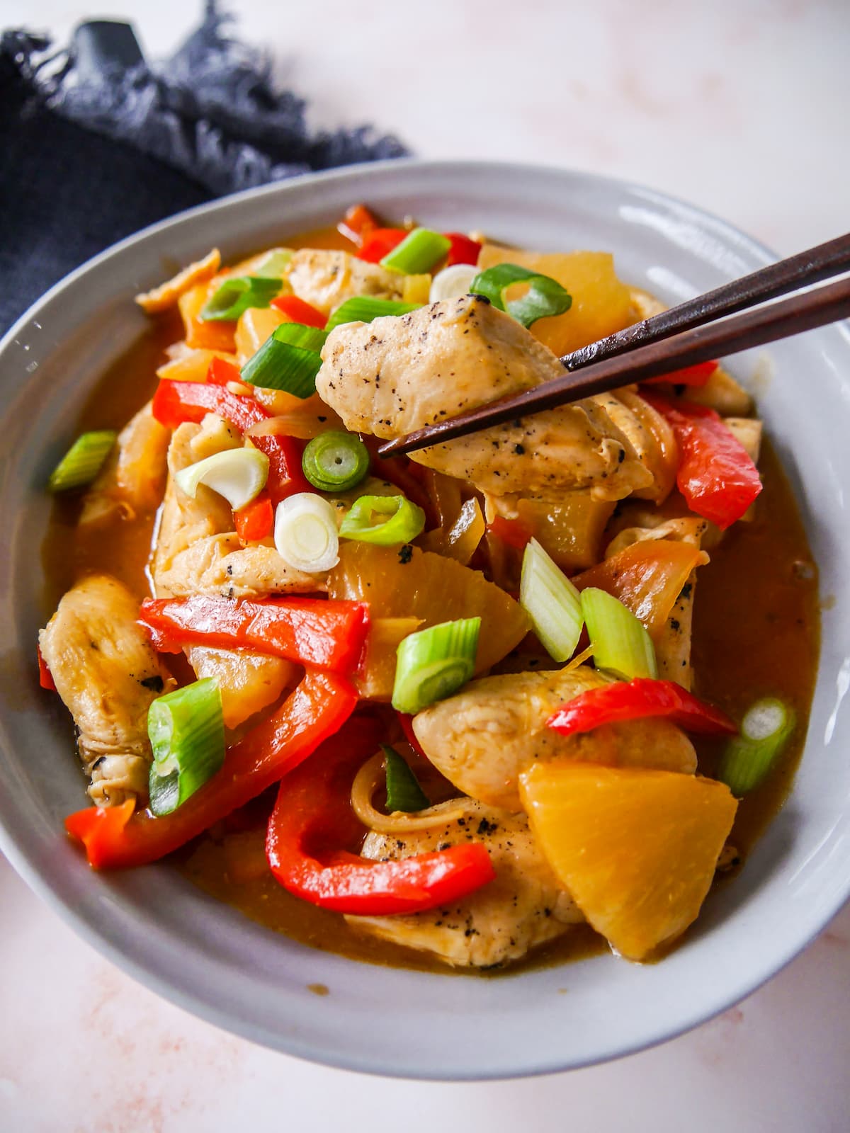 A bowl of sweet and sour chicken with stir-fried vegetables, with chopsticks holding a piece of chicken.