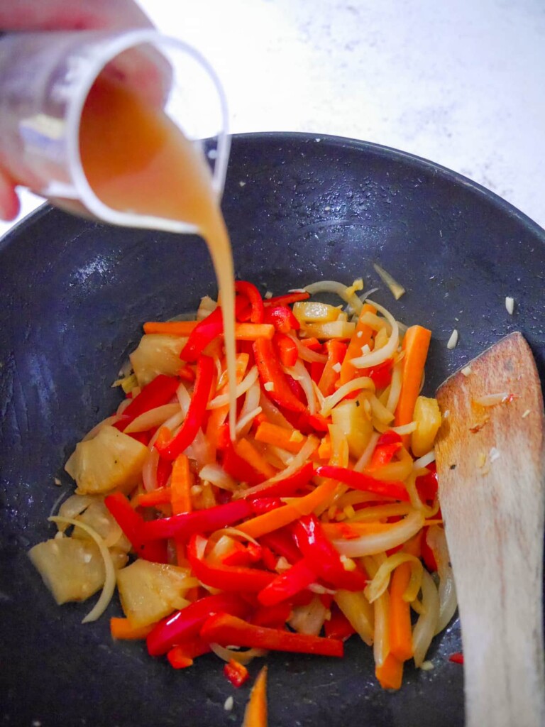 A wok with stir-fried vegetables with sauce being added.