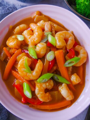 A pink bowl filled with sweet and sour prawn stir-fry, with a side of broccoli.