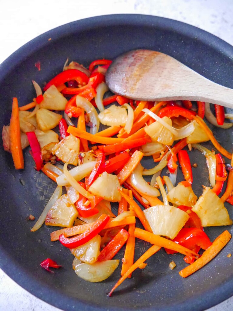 A frying pan with sauteed onion, carrot, red pepper, pineapple, garlic and ginger.