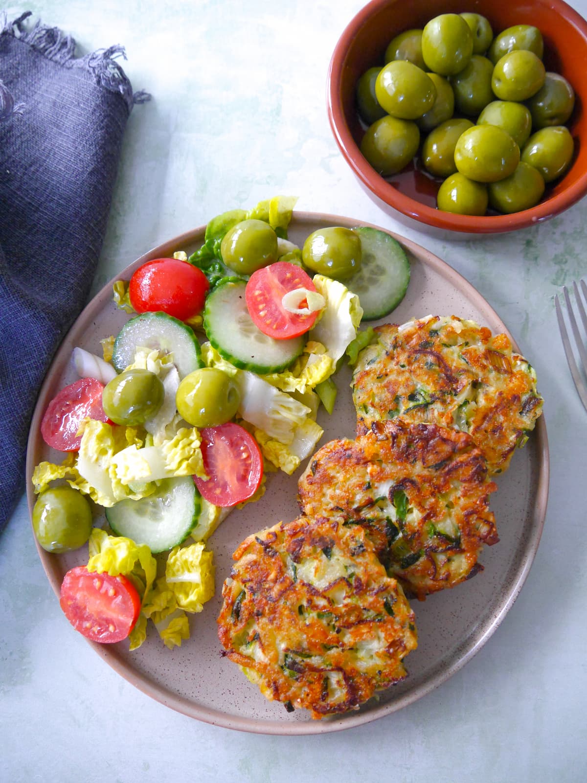 A plate with three courgette fritters and a side salad.
