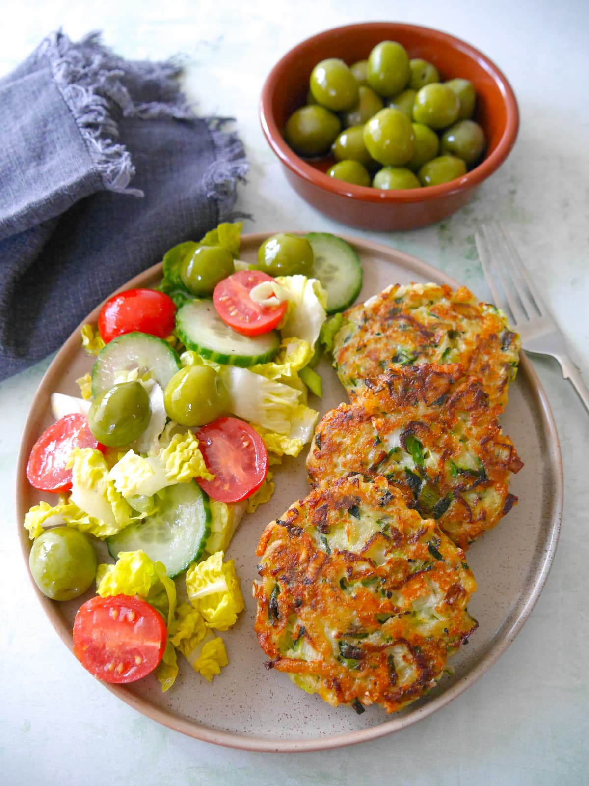 A plate with three courgette fritters and a side salad.