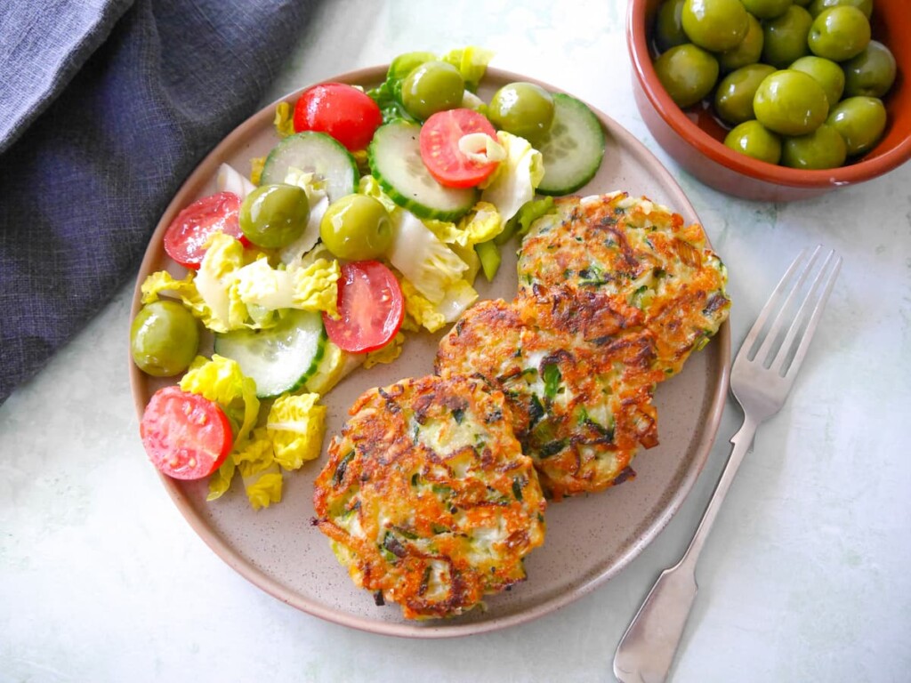 A plate with three courgette fritters and a side salad.