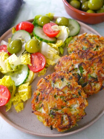 A plate with three courgette fritters and a side salad.