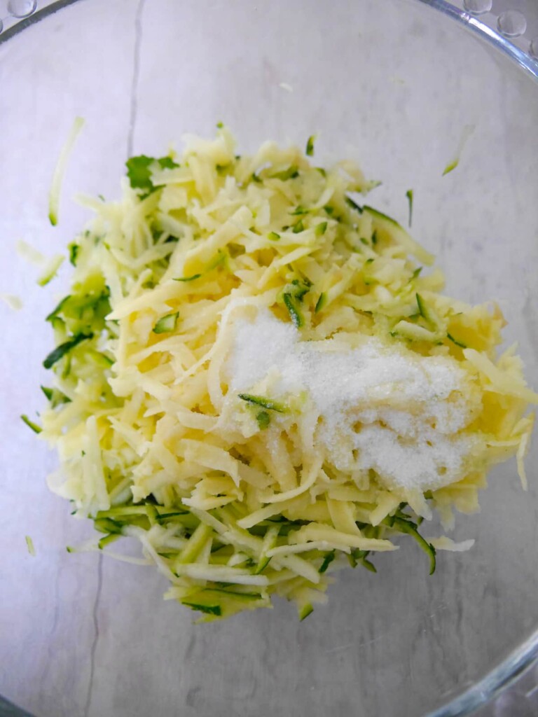 A bowl of grated courgette and potato with added salt to remove moisture.