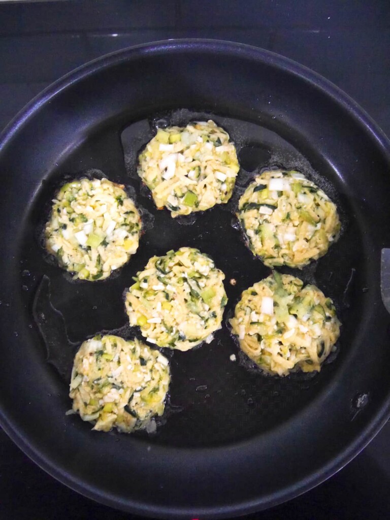 Courgette fritters being fried in a large non-stick frying pan.