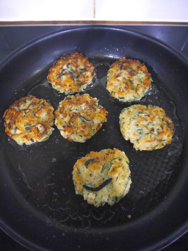Courgette fritters being fried in a large non-stick frying pan.