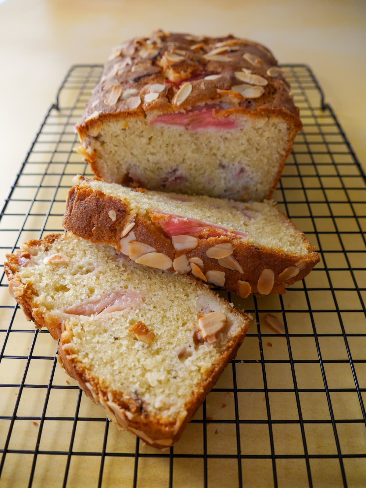 Rhubarb and almond loaf cake, with two slices of cake, set on a wire cooling rack.