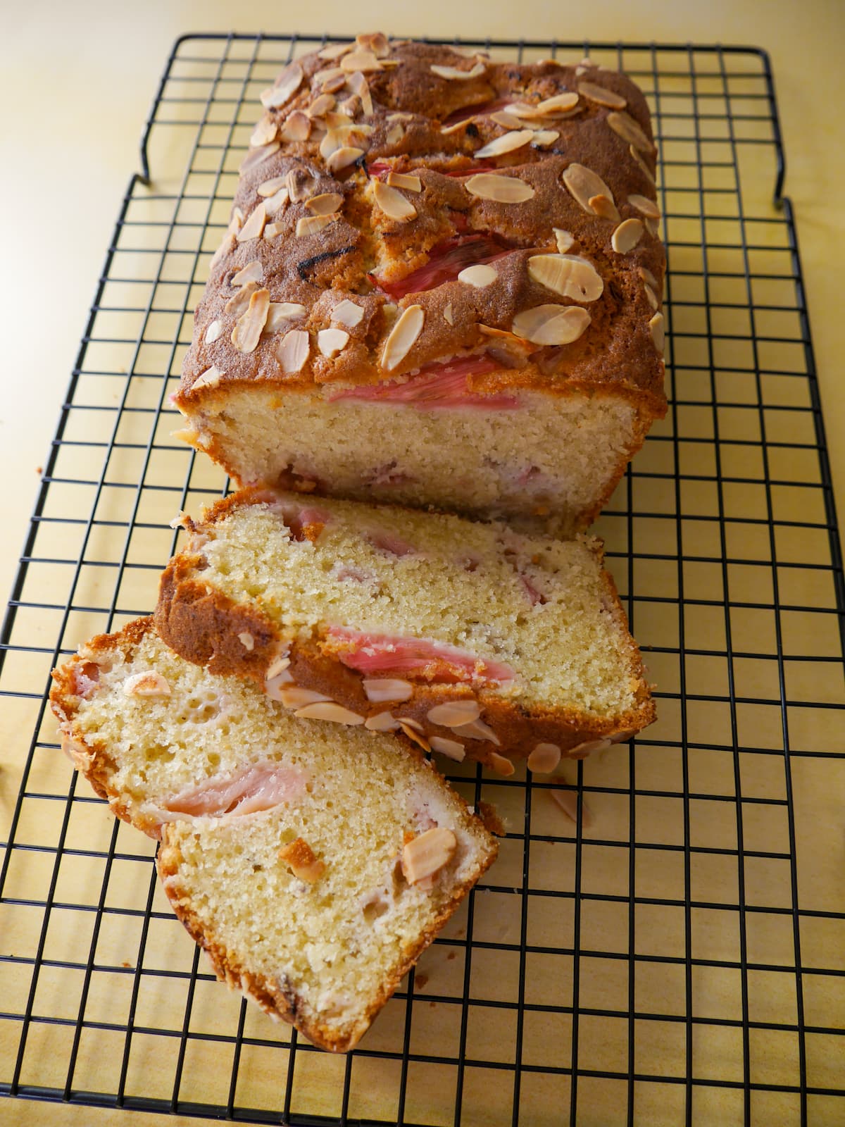 Rhubarb and almond loaf cake, with two slices of cake, set on a wire cooling rack.