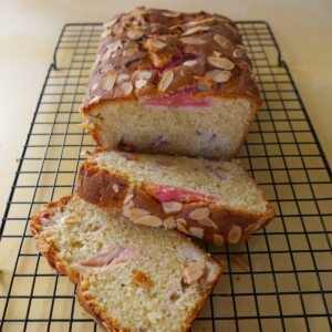 Rhubarb and almond loaf cake, with two slices of cake, set on a wire cooling rack.