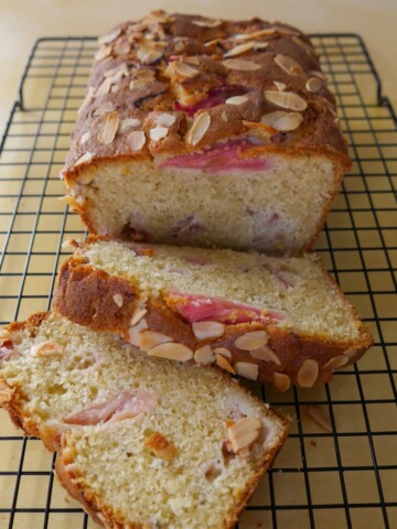 Rhubarb and almond loaf cake, with two slices of cake, set on a wire cooling rack.