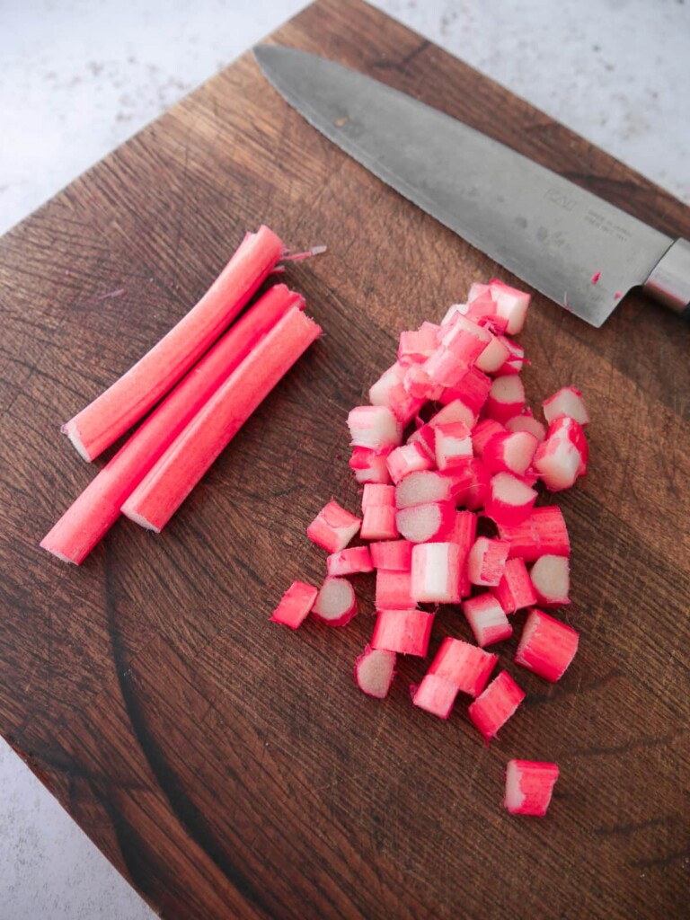 A wooden chopping board topped with stems of rhubarb, and finely diced rhubarb.
