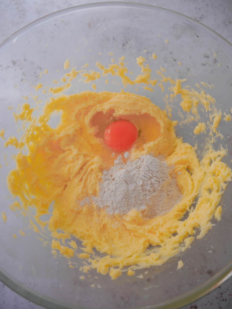 A large mixing bowl with creamed sugar and butter, with added egg and a spoon of flour.