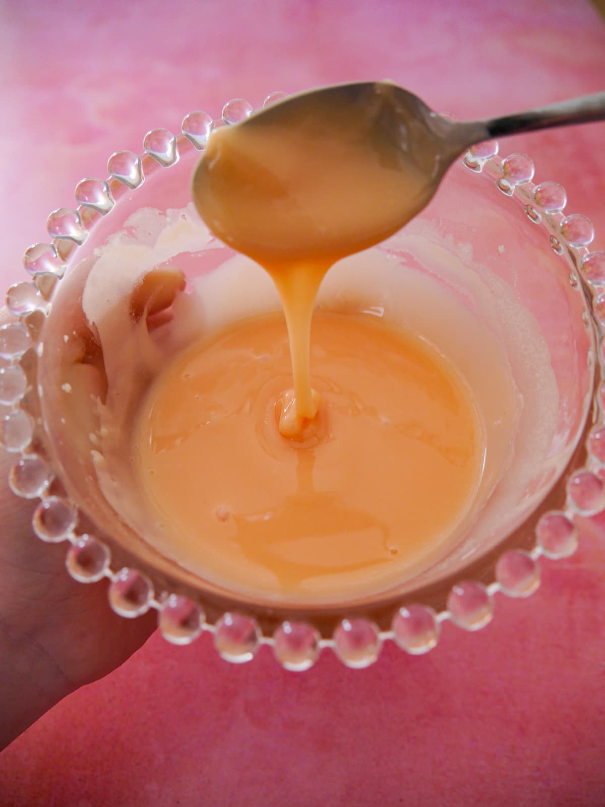 A hand holding a bowl of rhubarb and orange glaze icing.