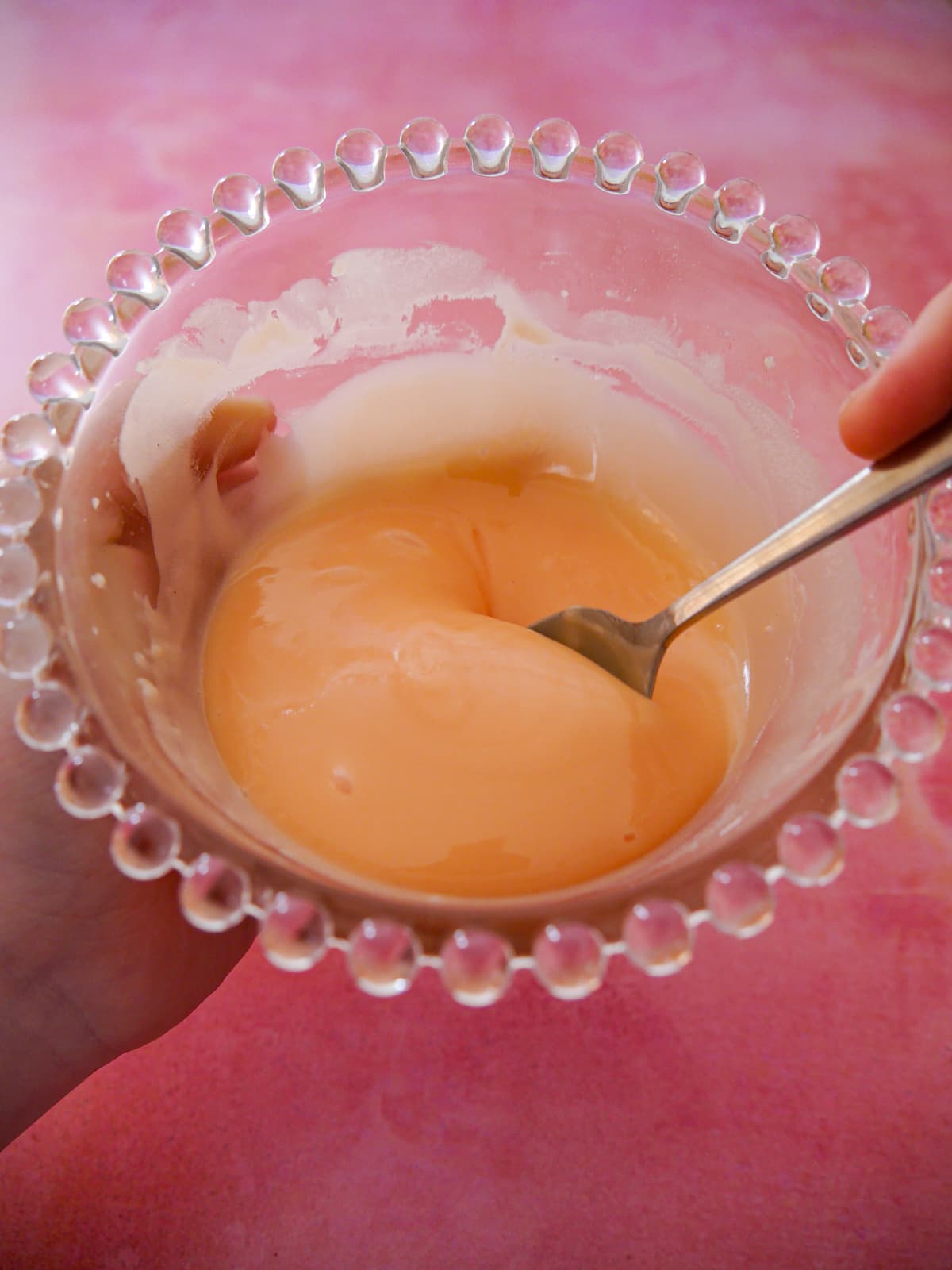 A hand holding a bowl of rhubarb and orange glaze icing.
