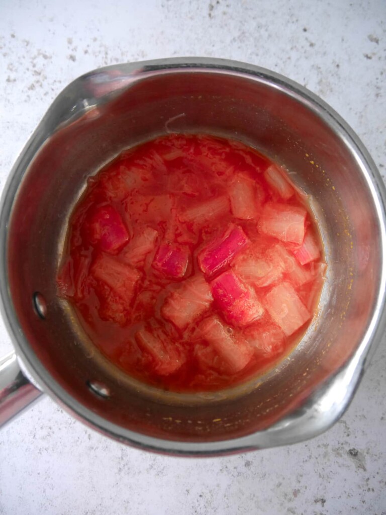 A saucepan with soft stewed rhubarb in an orange sauce.