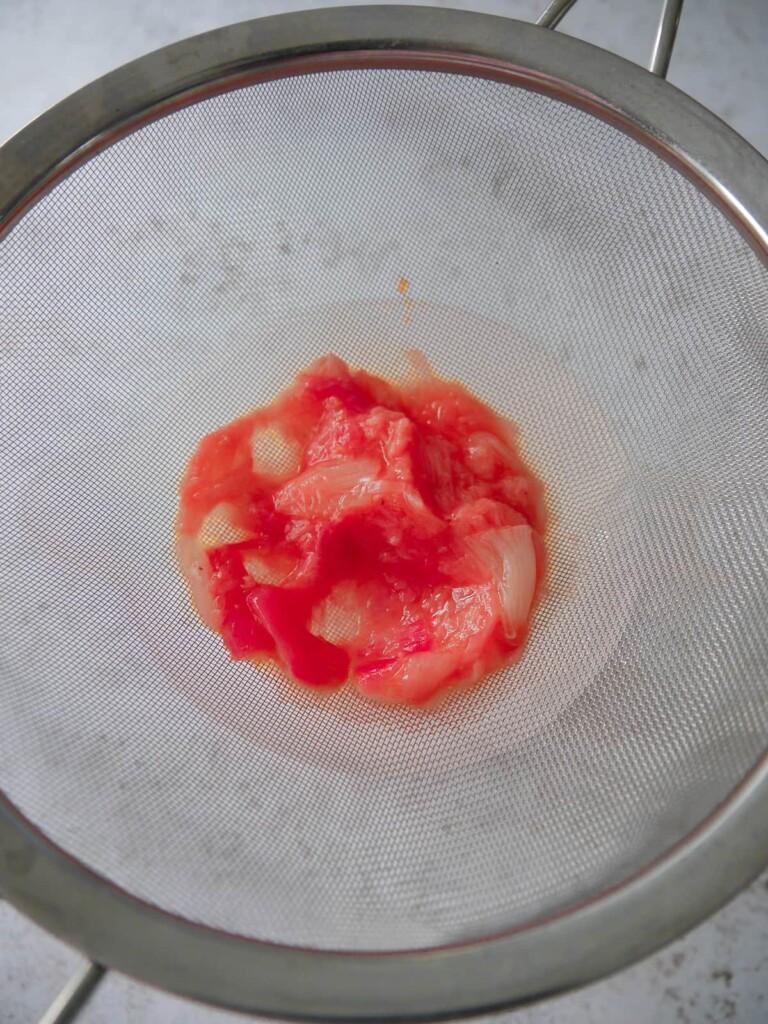 Stewed rhubarb being passed through a fine sieve to separate out the fruit juice.