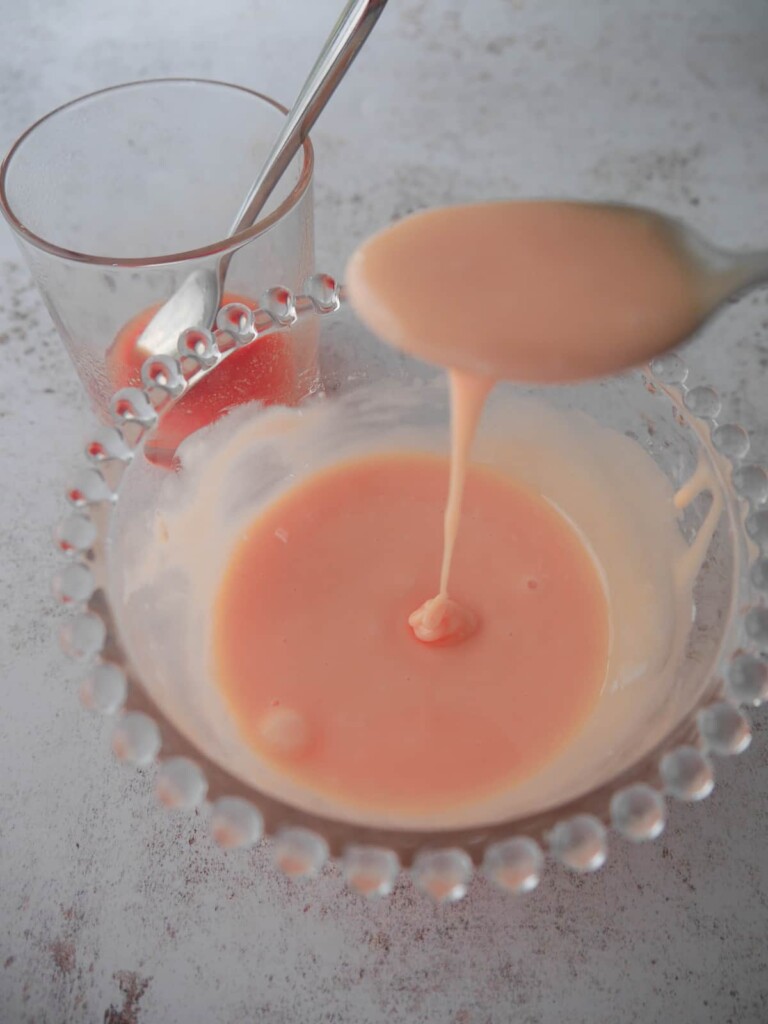 A bowl of combined rhubarb and orange glaze icing, with a glass of juice set alongside.