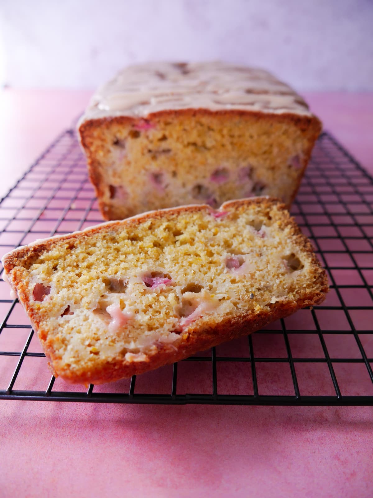 Rhubarb and orange loaf cake with a slice cut, set on a wire cooling rack.