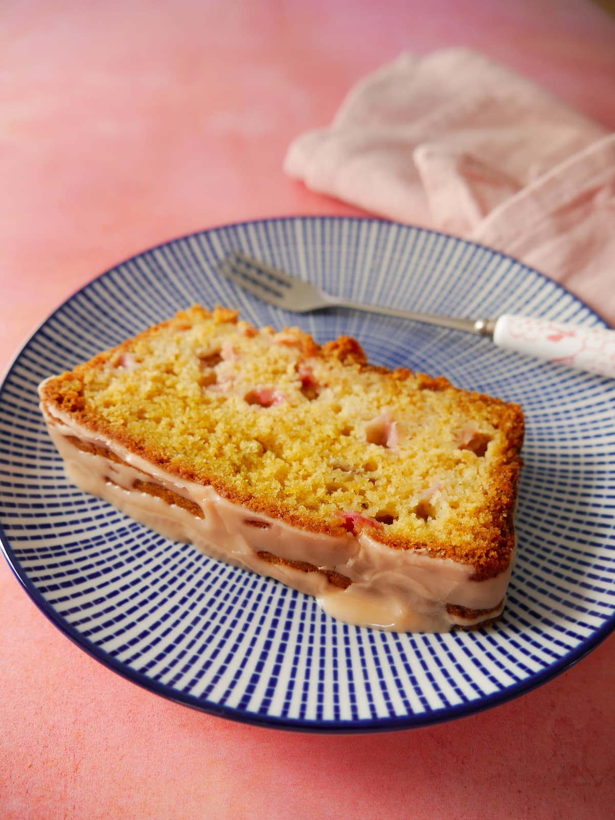 A plate with a slice of rhubarb and orange loaf cake, with a cake fork and napkin.