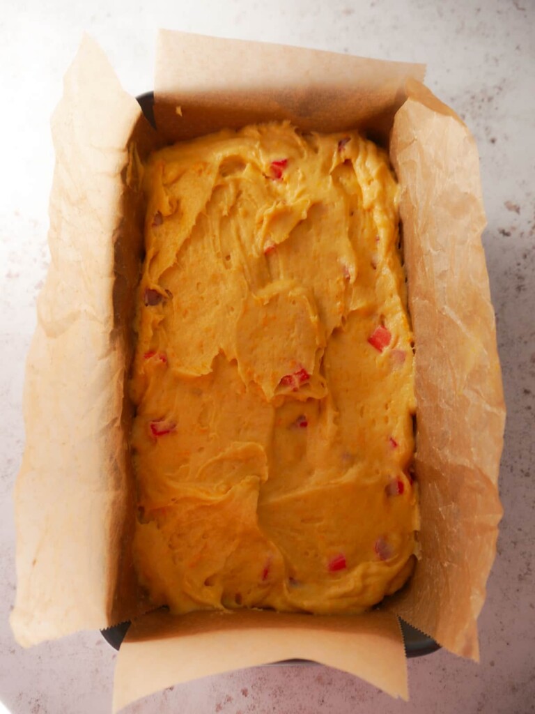 A lined loaf tin filled with rhubarb and orange cake batter.