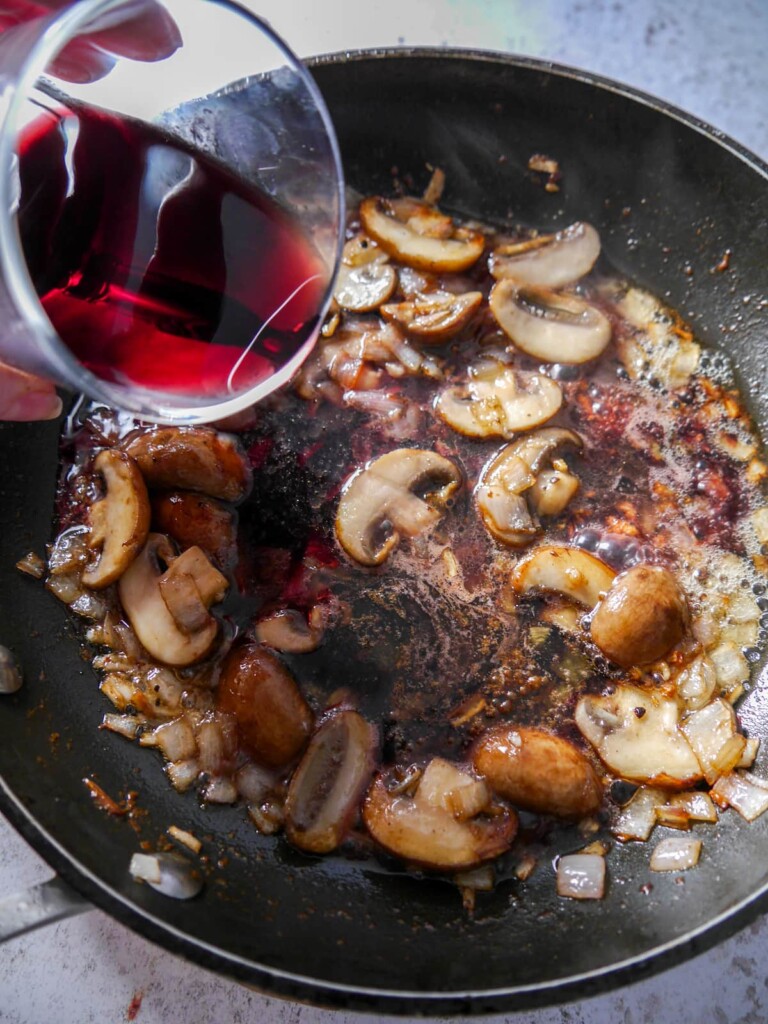 A frying pan of sauteed mushrooms, shallot and garlic with red wine being added.