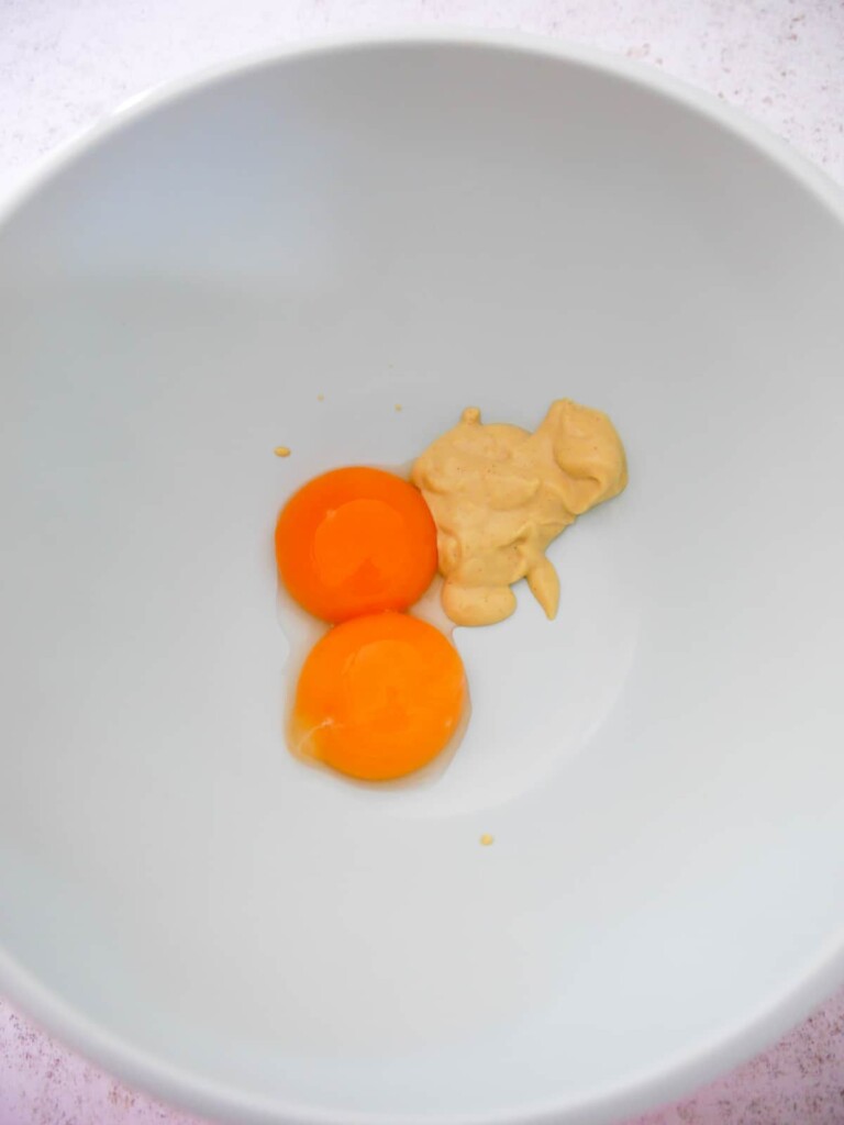 A bowl with 2 egg yolks and a tablespoon of Dijon mustard.