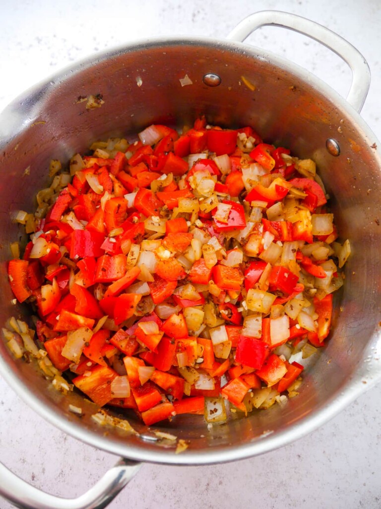 A large saucepan filled with sauteed onion, red pepper, chilli and garlic.