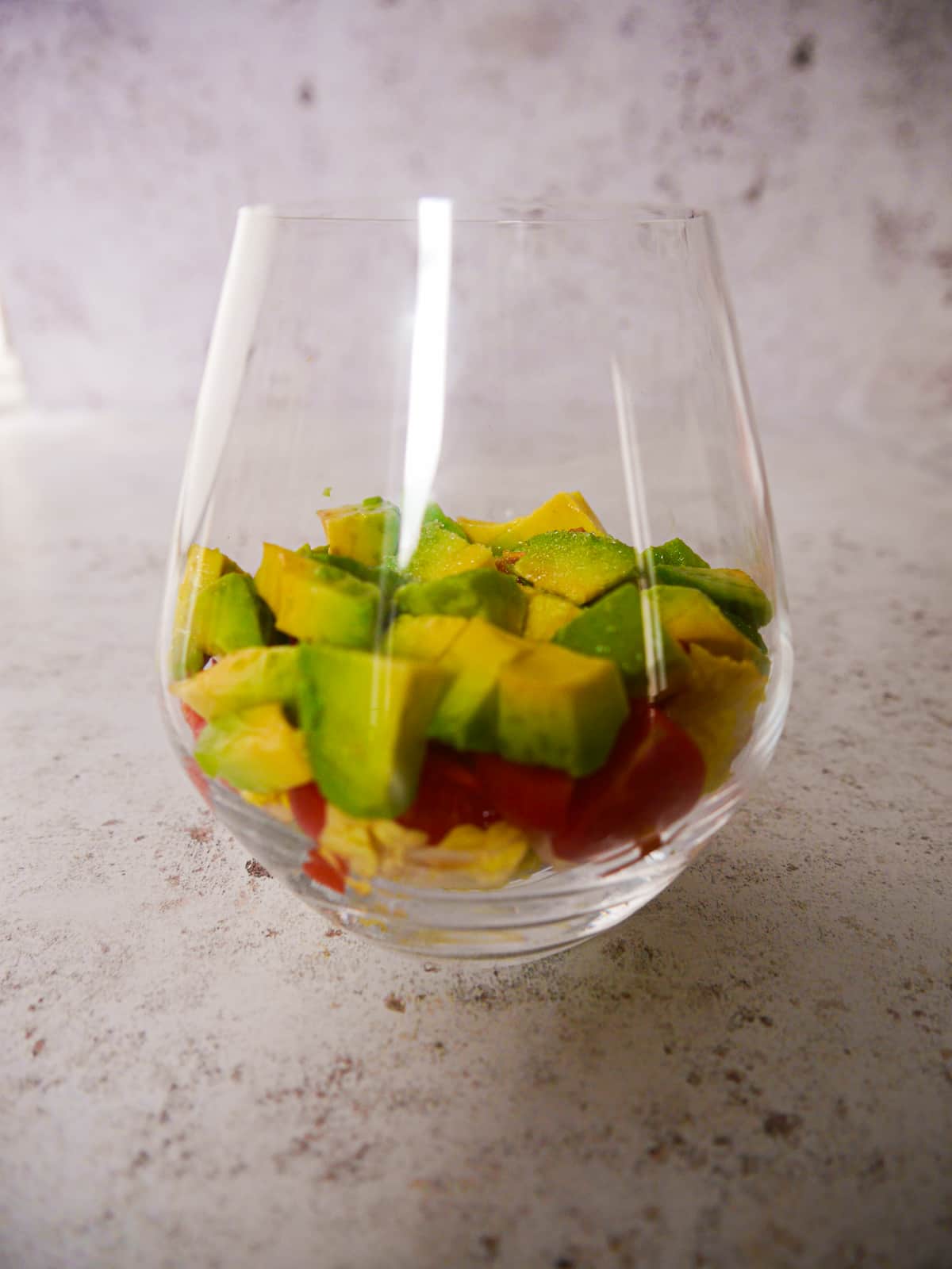 A large glass filled with a base of shredded lettuce, chopped tomato and avocado.