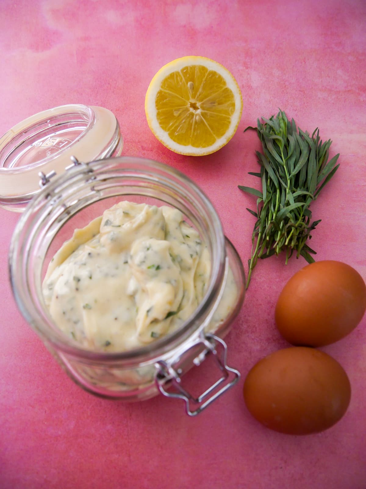 A jar of tarragon mayonnaise set aside 2 brown eggs, a lemon and stalks of fresh tarragon.