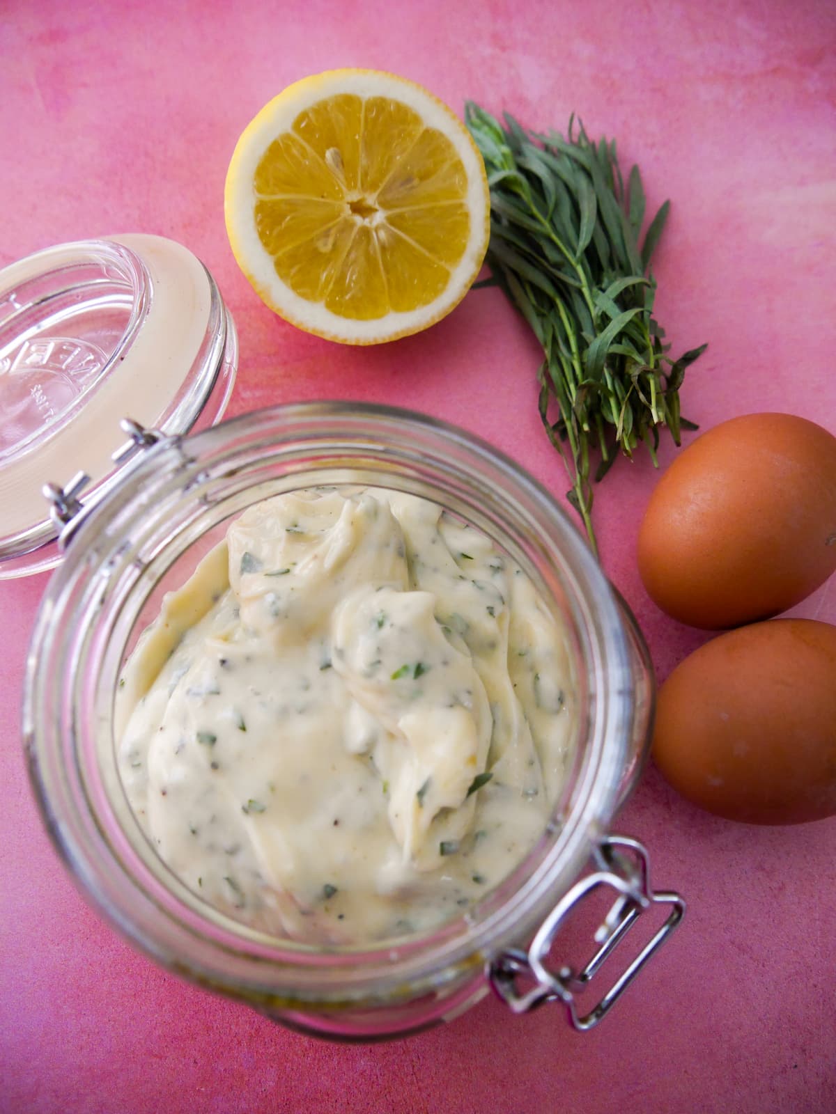 A jar of tarragon mayonnaise set aside 2 brown eggs, a lemon and stalks of fresh tarragon.