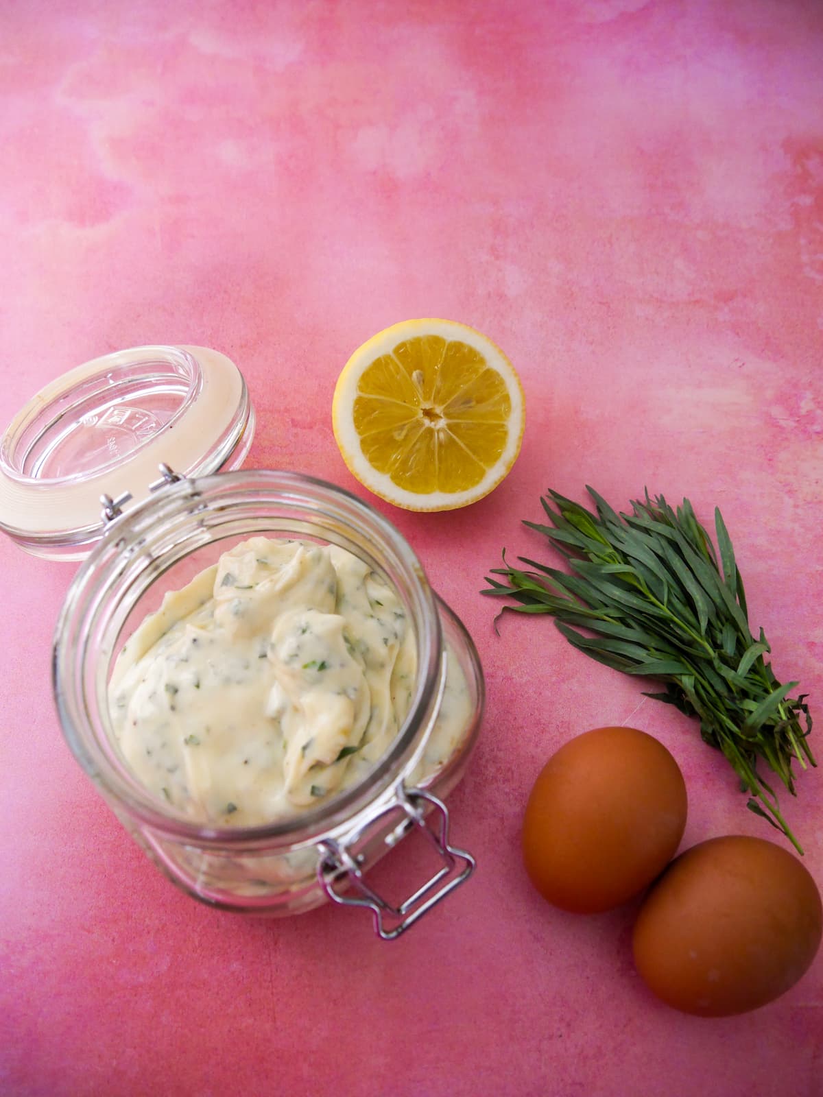 A jar of tarragon mayonnaise set aside 2 brown eggs, a lemon and stalks of fresh tarragon.