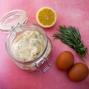 A jar of tarragon mayonnaise set aside 2 brown eggs, a lemon and stalks of fresh tarragon.